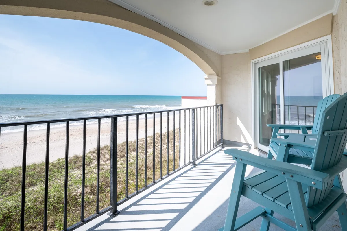 A private oceanfront balcony with classic Adirondack chairs, railings, and a panoramic view of the Atlantic Ocean. The scene evokes feelings of relaxation, capturing the essence of morning coffees, evening toasts, or quiet stargazing as described in the narrative.