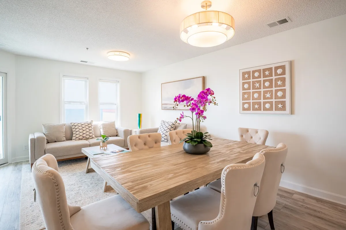 A bright, inviting dining area with a table featuring a floral centerpiece, a comfortable sofa with patterned cushions, and expansive windows that fill the space with natural light. The layout encourages togetherness and is ideal for shared meals and family activities.
