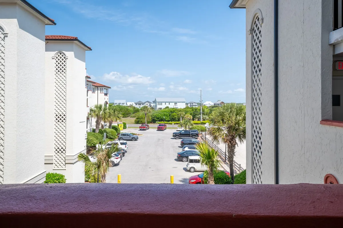 A view from a private balcony, with a railing in the foreground, overlooking the property’s palm trees, surrounding buildings, and the parking lot. The tranquil mood suggests a relaxing spot to unwind after a day of adventure.