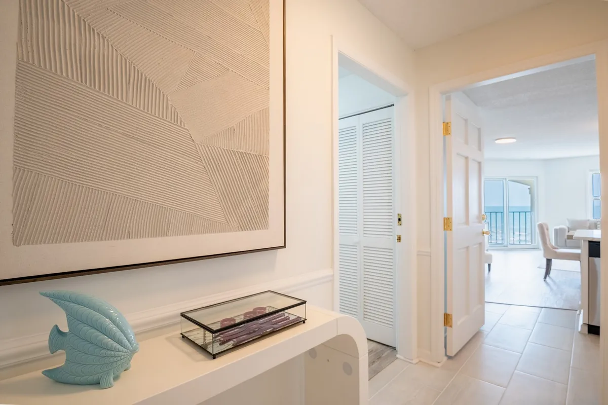 This image showcases the villa's entryway, featuring textured wall art, a decorative blue sculpture, and a transparent display box. The scene feels inviting and highlights the first welcoming impression guests receive when arriving, suggesting a warm and communal environment perfect for families and groups.