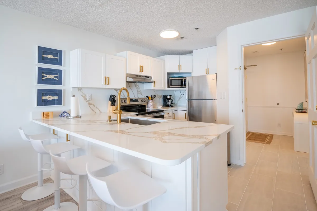 A bright and modern kitchen scene with a granite countertop, gold fixtures, crisp white cabinetry, and blue decorative accents. The space is open and airy, with plenty of surface area for food prep and room for hosting or casual dining.
