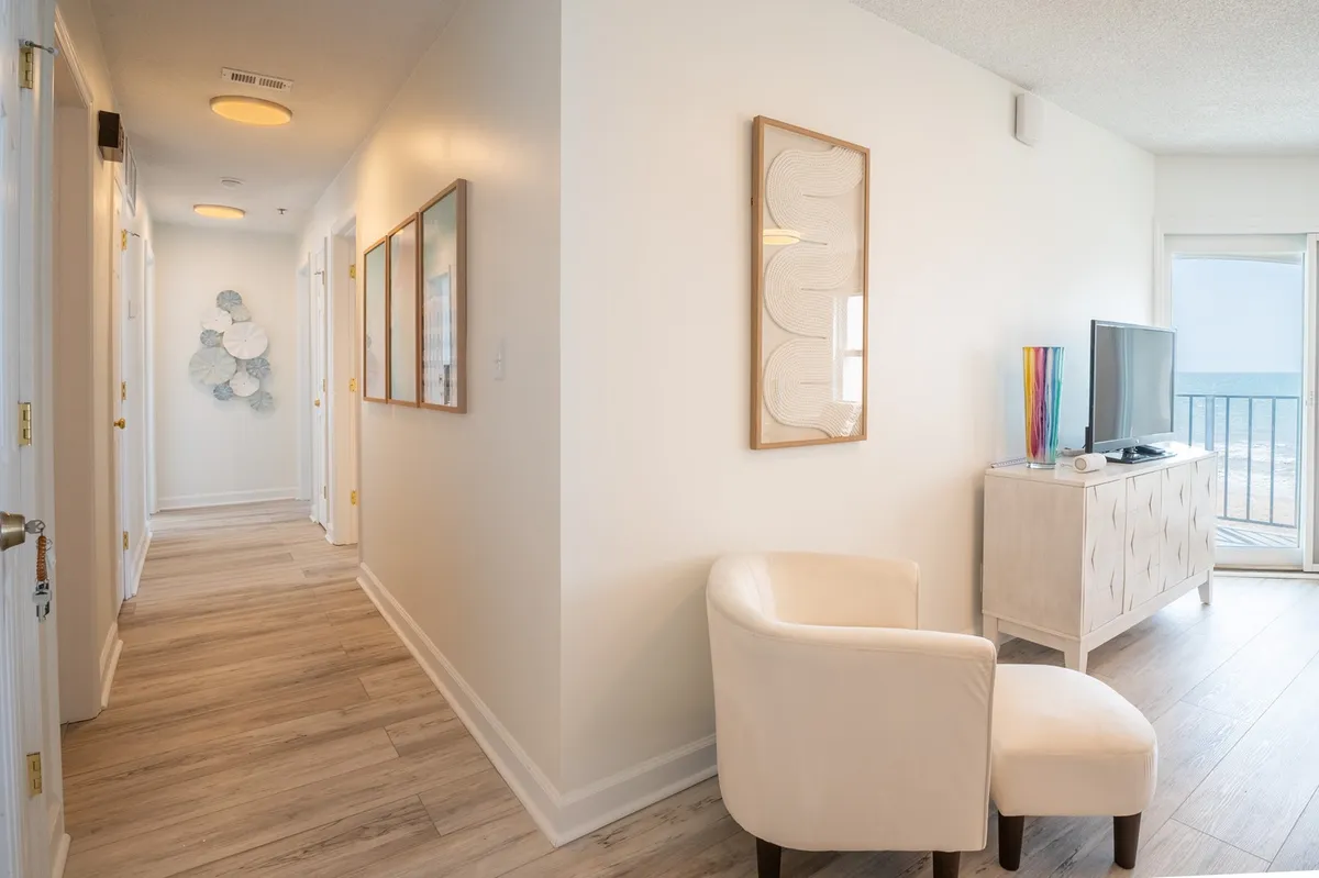 This image highlights a comfortable seating area with an armchair, TV stand, wall art, and a window view that hints at the coastal surroundings. The mood is calm and inviting, suggesting moments spent relaxing and enjoying the scenery after a day of exploring.
