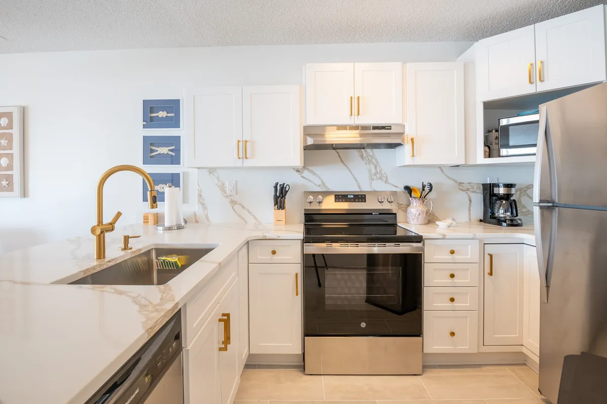 A modern kitchen featuring a sleek island with a gold faucet, a black stove, white cabinetry with gold accents, and decorative wall art. The layout highlights the kitchen island as a central prep and gathering area, with premium fixtures and finishes throughout, including ample counter space.