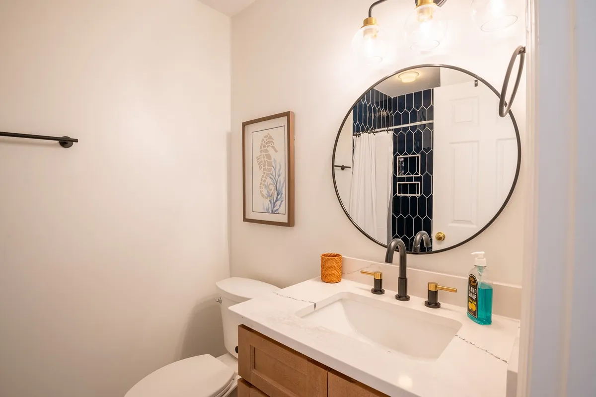 A modern and inviting bathroom with a round mirror, sleek sink, artistic wall decor, and hexagonal tilework. The space feels fresh, well-lit, and ideal for personal routines or getting ready for the day.